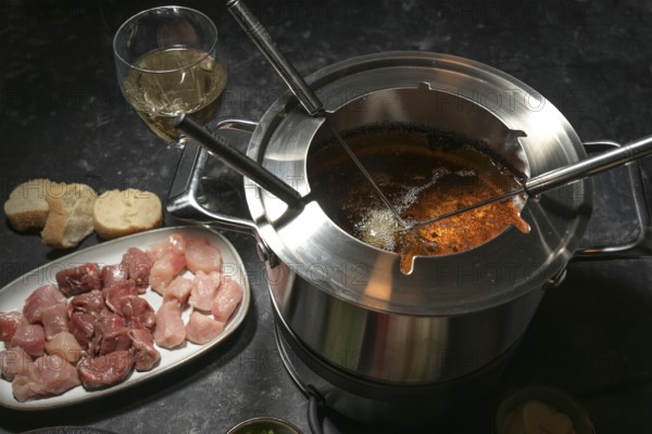 Fondue pot with boiling hot oil, long forks and raw meat, party dinner for friends and family,