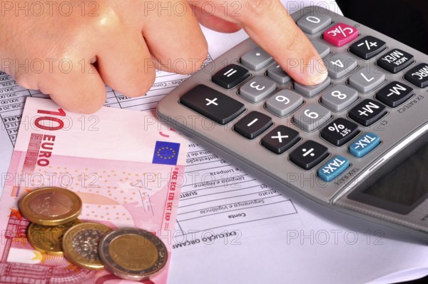 Business person doing accounts using a calculator with some money on the side