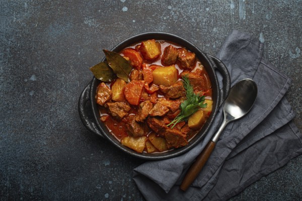 Beef meat stew with potatoes, carrot and delicious gravy in black casserole pot with bay leaves and