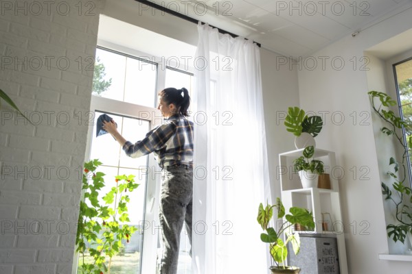 Woman manually washes the window of the house with a rag with spray cleaner and mop inside the