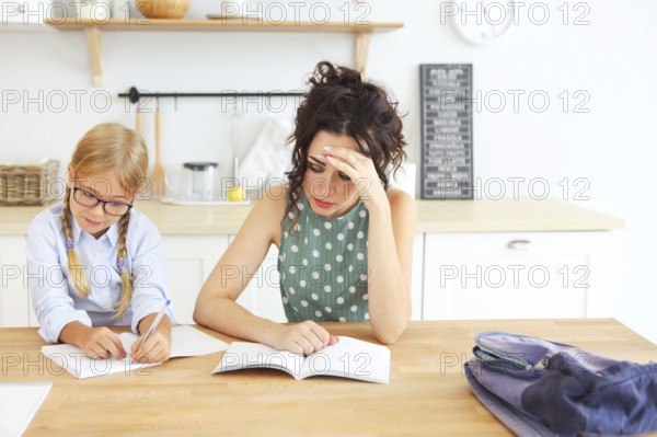 ?ute school girl wearing eyeglasses doing homework with mother at home on the kitchen