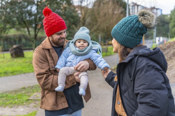 Parents holding their baby while enjoying a winter day outdoors in a park, wearing warm clothes and