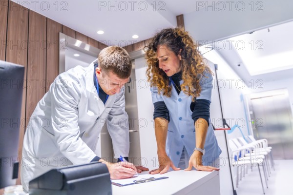 General practitioner doctor filling a form in the hospital next to a nurse