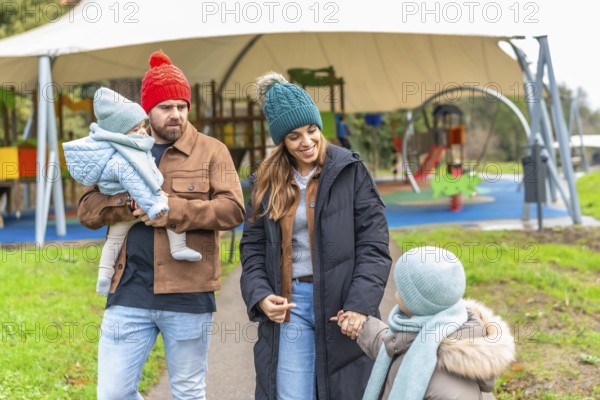 Happy family enjoying a winter day at the playground, bundled up in warm clothes and colorful hats,