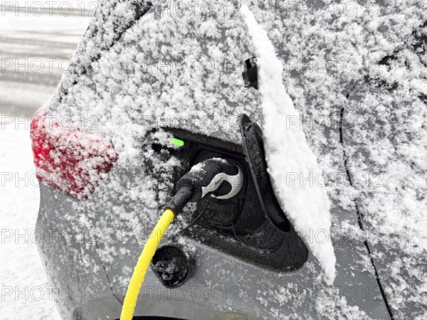 Charging an electric vehicle in winter. A yellow charging cable is connected to the car's charging