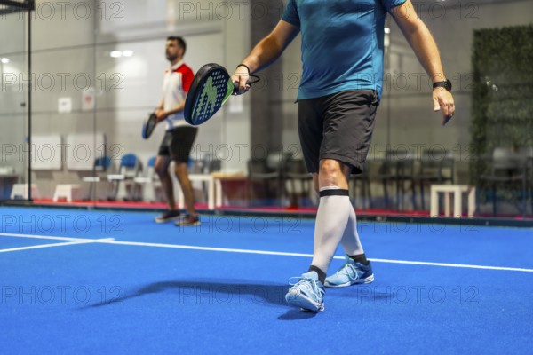 Team of two male mature friends playing paddle tennis in an indoor court