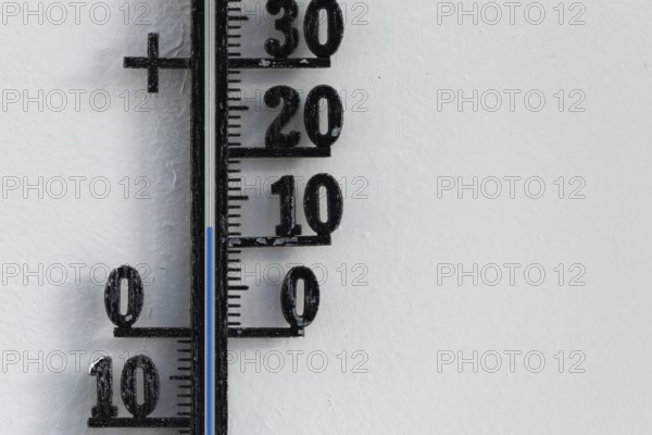 Classic analog thermometer hanging on white wall displaying warmth of twelve degrees celsius