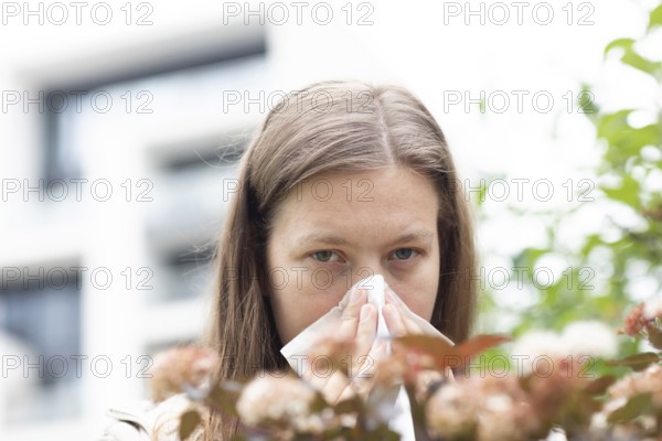 Young woman suffers from hay fever and uses a paper handkerchief outdoors, Freiburg,