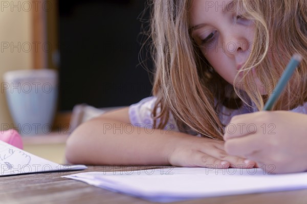 Close-up of a beautiful blonde girl in a colorful dress concentrating on school homework