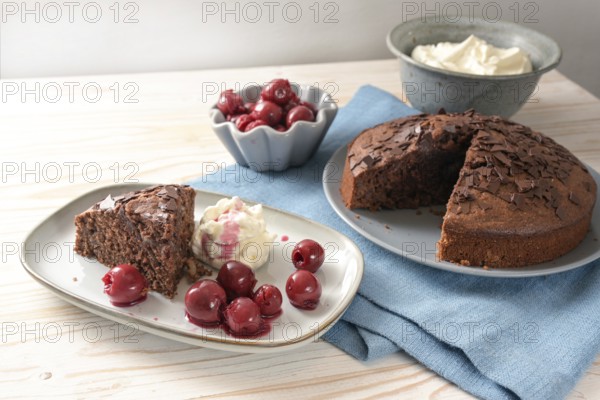 Homemade chocolate cake with morello cherries and whipped cream on a blue napkin and a bright