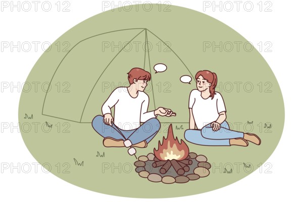 Happy man and woman sitting near campfire in forest. Smiling couple relax at wood camp near fire