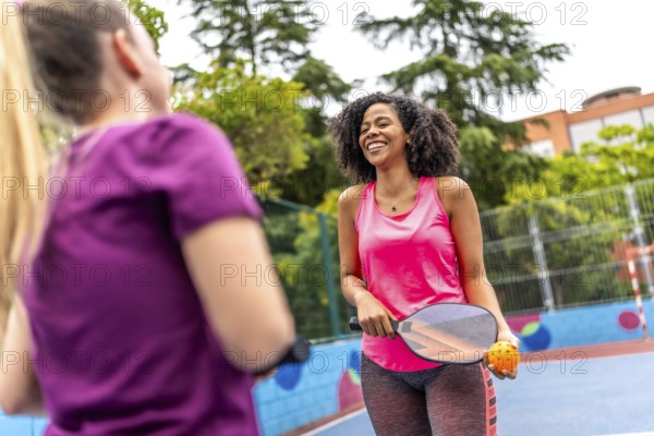 Happy pair of multi-ethnic women playing pickelball in an outdoor court