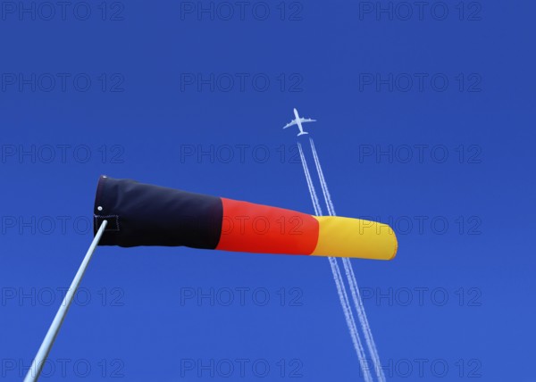 A passenger plane with vapour trails high in the blue sky and a german windsock