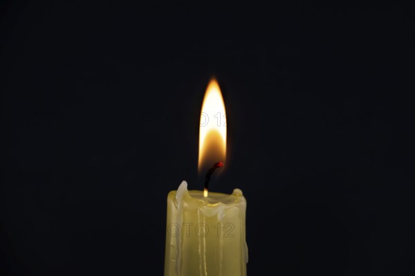 Burning yellow wax candle contrasting with the dark background, candle's gentle flame suggesting of