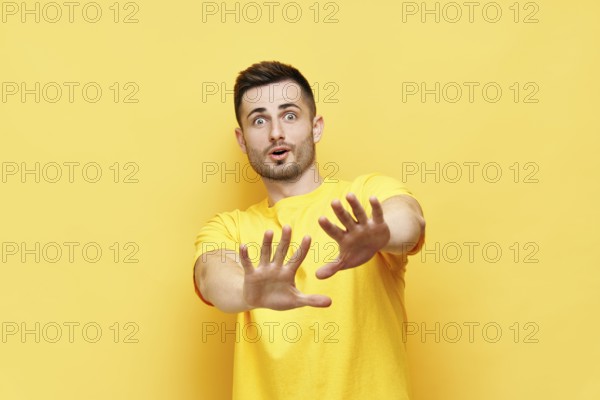 Young displeased man making stop gesture sign say no isolated on yellow background. Negative
