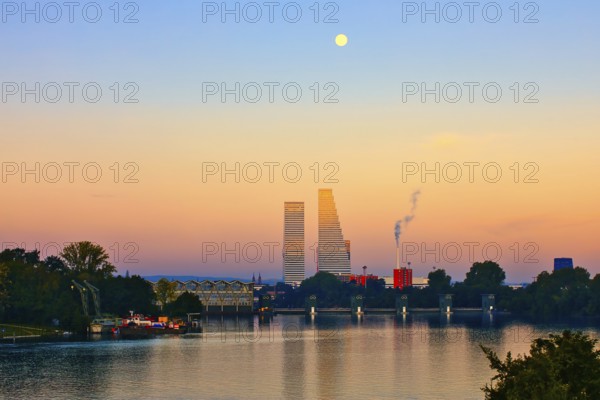 River landscape at sunset with skyscrapers and full moon. The scene contains natural and industrial