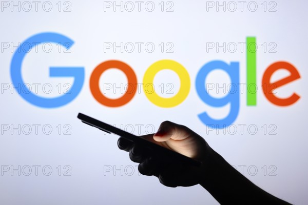 In this photo illustration the Google logo seen in the background of a silhouette hand holding a