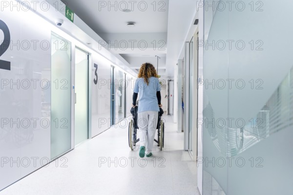 Rear view of nurse pushing a wheelchair along the hospital with a mature woman sitting on it