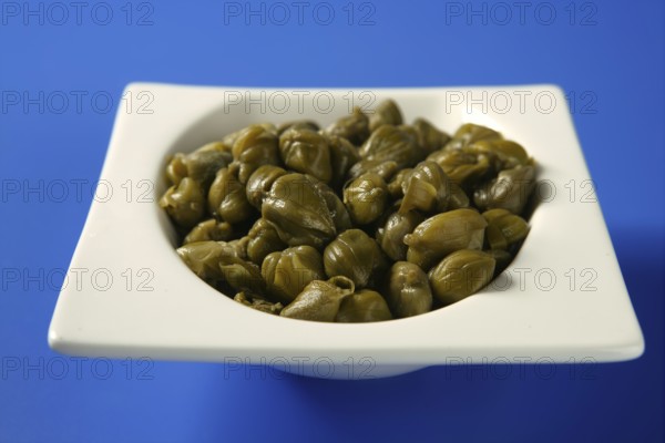 Capers with vinegar snack on a white plate, blue background