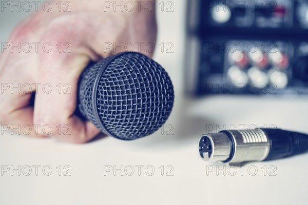 Close up picture of holding in hand microphone and audio cable, mixer in the blurry background