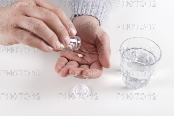Male hands with bottle of pills and glass of water over white table
