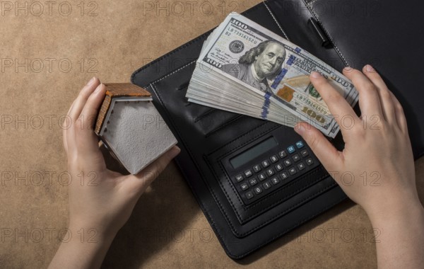 Hand holding house beside American dollar banknotes and globe