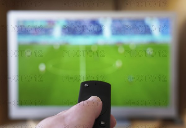 hand pointing remote control at tv set with soccer or football match