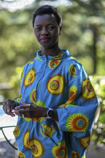 Young adult afro hair diverse model in traditional attire smiles softly while holding sunglasses