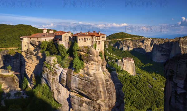 Clifftop Varlaam monastery lit by evening sunlight in Meteora, Greece in typical Meteora landscape
