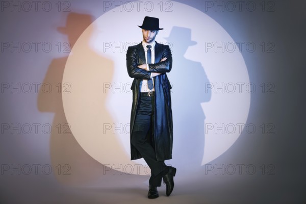 Full length portrait of confident handsome man in black coat and hat with crossed arms posing on