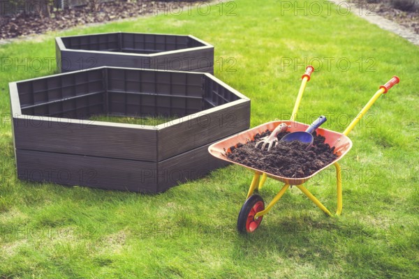 Garden barrow with soil and empty raised beds on grass prepared for filling with soil. Urban