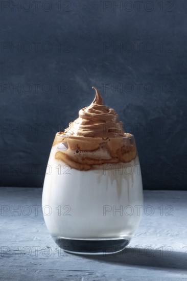 Dalgona cold coffee in a glass on a dark blue background with copy space. Trendy Korean milk shake