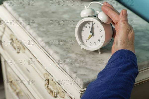 Woman in bed puts out her arm to turn off the alarm clock in the morning