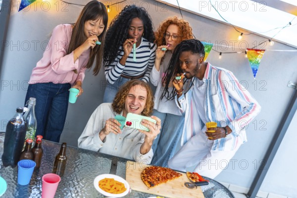 Happy caucasian man taking selfie surrounded by multi-ethnic friends blowing streamers during