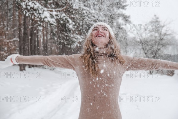 Christmas, holidays and season concept. Young happy woman blowing snow in the winter forest nature.