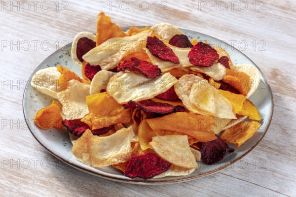 Vegetable chips on a plate, a healthy vegan snack on a wooden background
