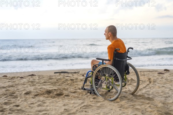 Portrait a disabled person on his back in a wheelchair on the beach with open arms enjoying the