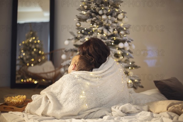 Family traditions. Mother and little boy son watching Christmas movie or tv with popcorn at home,