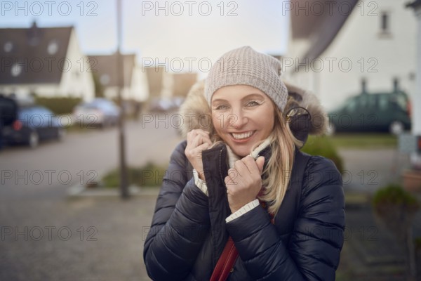 Smiling happy middle-aged woman standing outdoors on a cold winter day in a warm jacket and knitted
