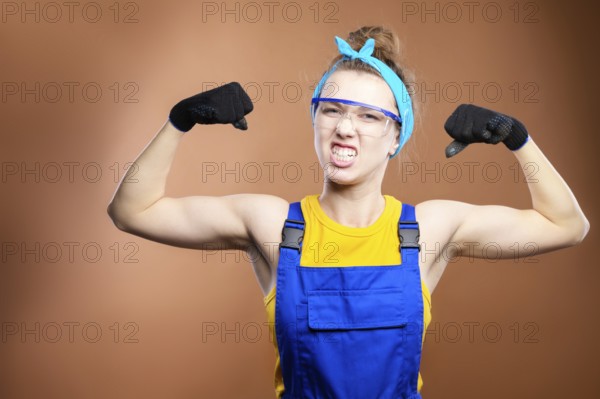 Young beautiful caucasian woman repairman worker with blue eyes in uniform showing arm muscles,