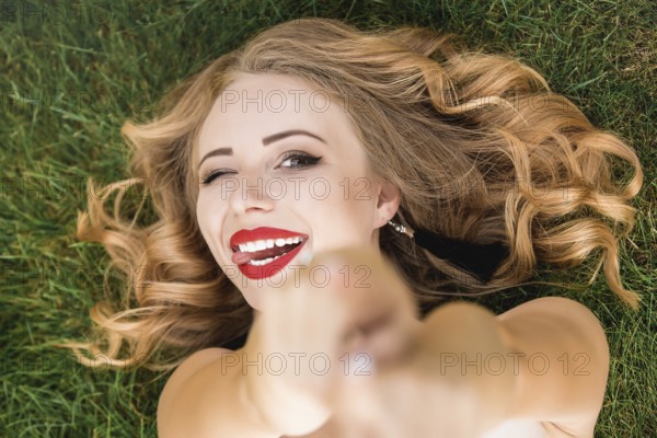 Caucasian pretty woman with curly black hair lying on the grass in the park. Smile and calm.