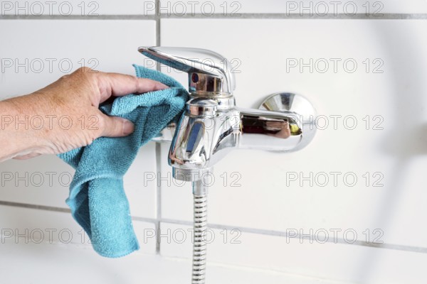 Cleaning a bathtub faucet with a blue microfiber cloth to remove limescale stains from hard calcium