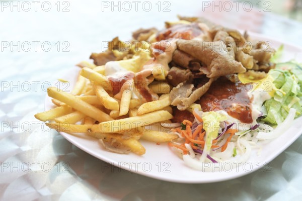 Doner kebab on a plate with French fries, salad and various sauces on a plate, popular fast food