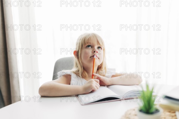 A little girl sits at the table and writes in a white notebook. Girl raised her finger, have an