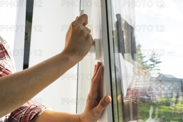 The hand holds the handle of a plastic double-glazed window, closing and opening the window with a