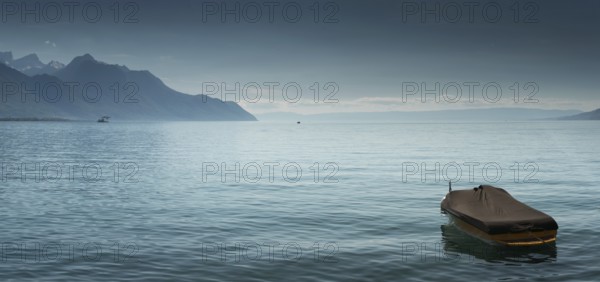 A beautiful view of Lake Geneva and surrounding mountains on a summer day with a single boat in the