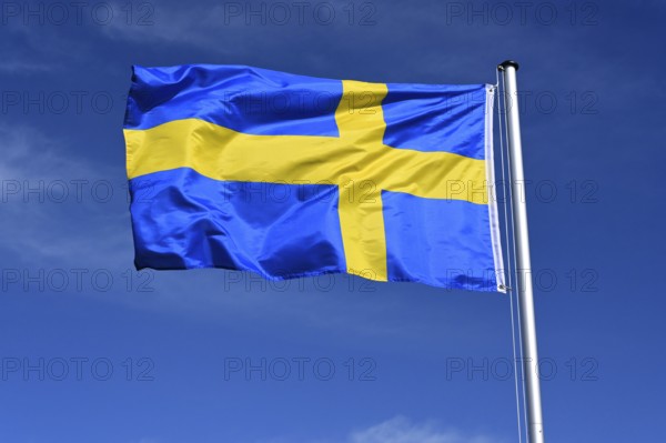 The flag of Sweden flutters in the wind against a blue cloudless sky