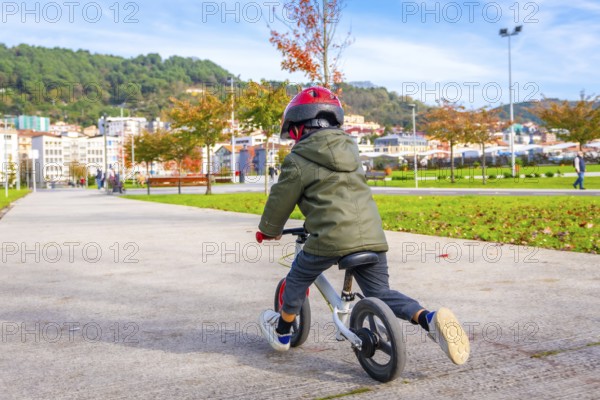 A young boy is riding a bicycle down a sidewalk. He is wearing a helmet and a green jacket