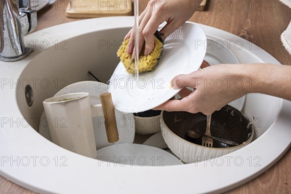 Women's hands wash the plate under the tap water. Dirty dishes in the sink in the kitchen, mess