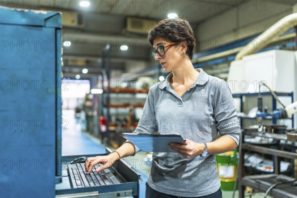 Female adult manager of a factory using computer while checking the quality of products and doing